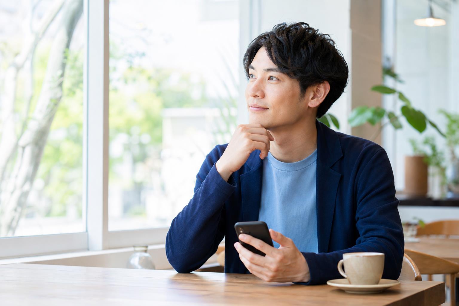 明るいカフェでスマートフォンを手に次の一歩を考える男性
